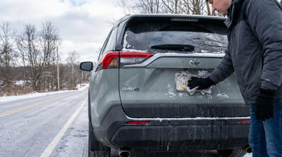 A gloved hand wiping snow from a car hire license plate during a winter day in Pennsylvania