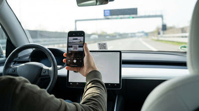 A hand holds a phone up to a QR code sticker on the dashboard of a car hire vehicle in California
