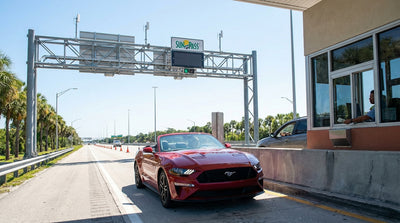 A modern car rental driving on a sunny Florida highway toward an electronic cashless toll gantry