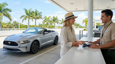 A sleek car rental cruises past Art Deco buildings on a sun-drenched street in Miami