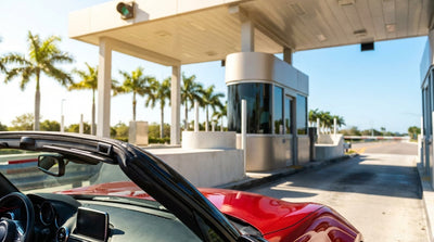 A white sedan car rental driving on a sunny Florida highway towards an overhead toll sign
