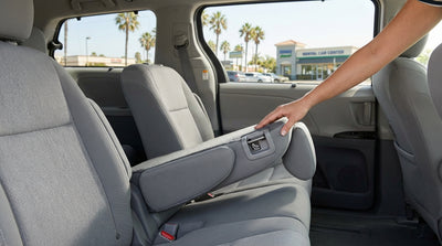 A parent leans into the back seat of a car rental to check child seat anchors in a sunny California lot