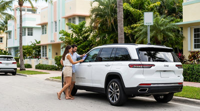 A stylish car rental parked on a sunlit residential street in Miami, shaded by lush green palm trees