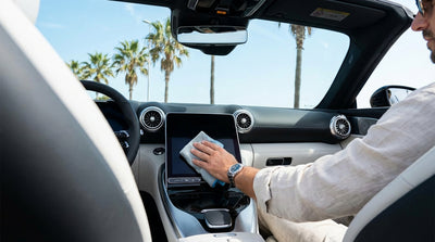 A person's hand on the touch screen of a modern car rental with a sunny Florida street in the background