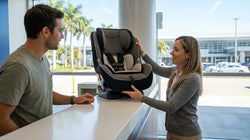A parent adjusting a child seat in the back of a car hire parked on a sunny Miami street