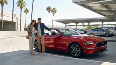 A modern convertible car hire parked on a scenic coastal highway overlooking the ocean in sunny California