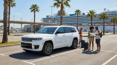A white convertible car hire driving along the water in Miami with a large cruise ship docked in the background