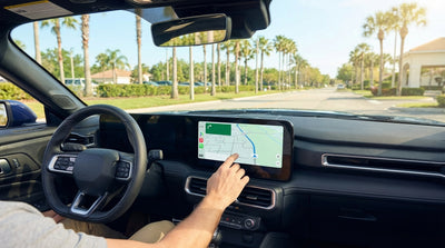 A driver's hands on a steering wheel viewing a car rental's built-in sat nav screen with a map of Orlando