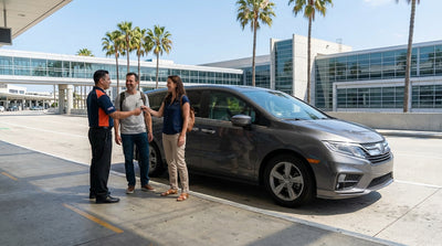 A woman smiling as she receives the keys for her car rental on a sunny day with California palm trees in the background