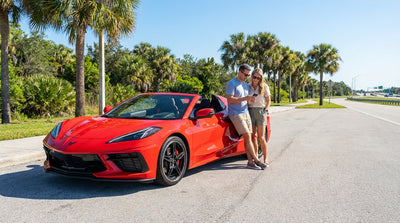 A convertible car hire drives down a scenic Florida highway lined with tall green palm trees