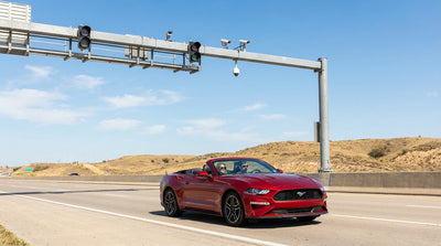 A car hire vehicle driving under an electronic toll collection gantry on a sunny multi-lane highway in Texas