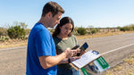 A driver inspects minor damage to their car rental vehicle on the side of a Texas road
