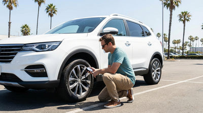 A person checking the tire pressure of a car rental sedan in a sunny California parking lot