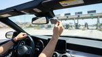 White car rental driving under a FasTrak electronic toll sign on a California highway