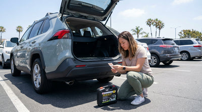 A person kneels to inspect the tyre of a modern car hire in a sunny California parking lot with palm trees