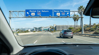 A silver car rental driving on a highway with the iconic San Francisco skyline and Bay Bridge at sunset