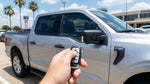 Close up of a hand pressing a key fob to unlock a silver car rental parked on a sunny street in Texas