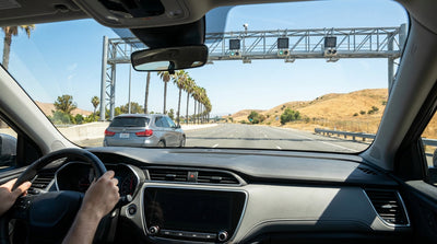 A car rental drives on a busy highway under a FasTrak toll gantry in Southern California