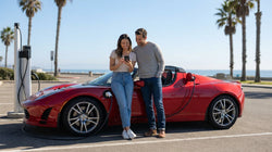 Person holding a smartphone beside an electric car rental at a charging station in California