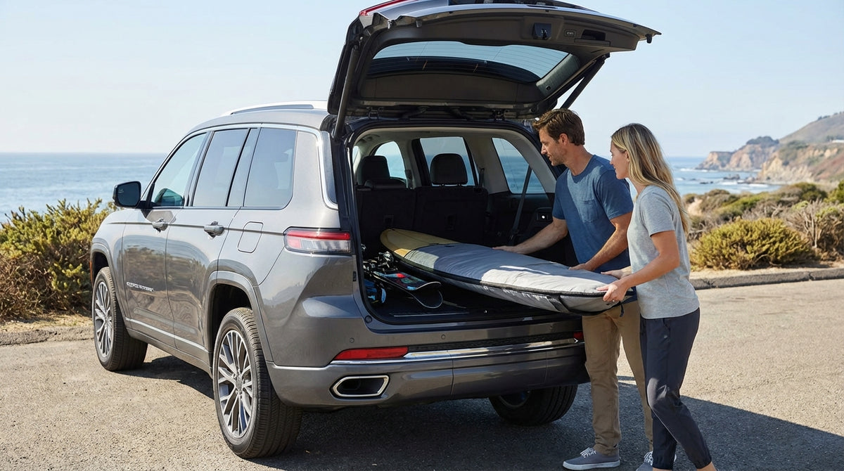 A surfer loading a surfboard into a car hire vehicle on a sunny California coastal road