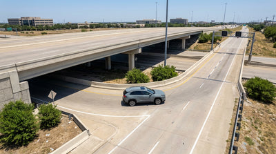 A car rental approaches the entrance to a Texas U-turn lane under a multi-level freeway interchange