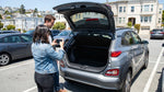 A woman looks into the open trunk of a car hire vehicle parked on a sunny street in San Francisco