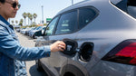 A driver stands by their car rental at a gas pump in California, looking at the fuel options