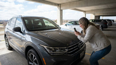 A silver car hire with hail damage on its hood parked on a rural road in Texas under a dark, stormy sky