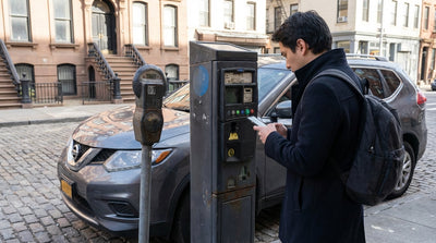 A gray car rental is parked on a city street in New York in front of a broken parking pay station