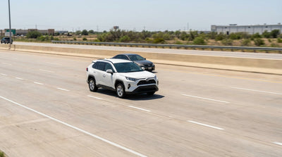 A modern car hire driving on a multi-lane highway under a big, sunny Texas sky