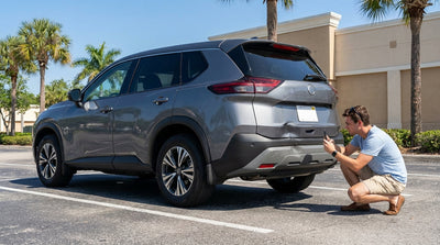 A white car hire with a dented fender parked on a sunny street lined with palm trees in Florida