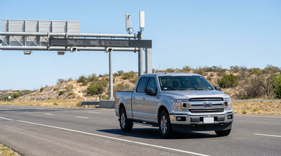 White car rental driving on a sunny Texas highway approaching a toll gantry