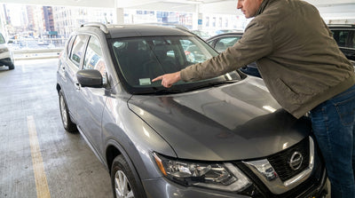 A close-up of the registration and inspection stickers on a car hire windshield with New York City streets blurred behind