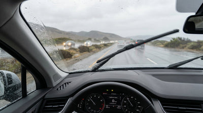 A car hire driving in the rain in California with its headlights and windshield wipers turned on