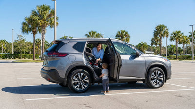A parent buckles a toddler into a car seat in the back of their car hire on a sunny day in Florida