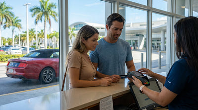 A smiling couple standing next to their red convertible car hire on a sun-drenched street in Miami