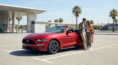A red convertible car rental drives down a long, empty desert highway in the United States at sunset