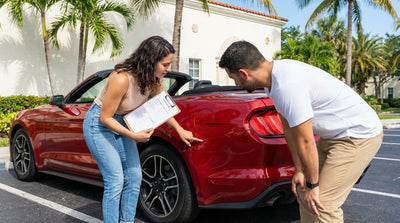 A person carefully inspects a white convertible car rental parked on a sunny street in Miami