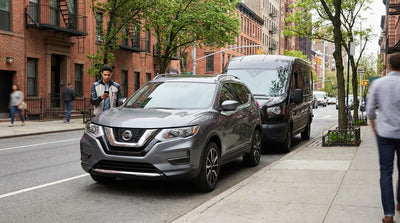 A car hire vehicle is blocked in by a double-parked car on a busy street in New York City