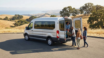 A large passenger van car rental parked on a scenic overlook of the California coast at sunset
