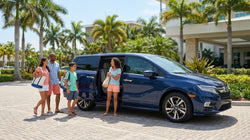 Two passengers smiling inside a car rental driving along a sunny Florida beach road