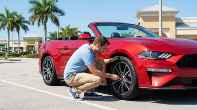 A driver inspects the tire of their car rental vehicle in a sunny Florida car park lined with palm trees
