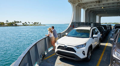 A white car rental on the deck of a car ferry crossing blue water under a sunny Florida sky