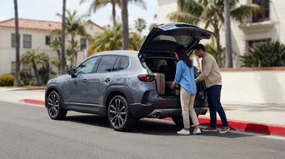 A car rental stopped next to a red painted curb on a sunny street in California with a person loading luggage
