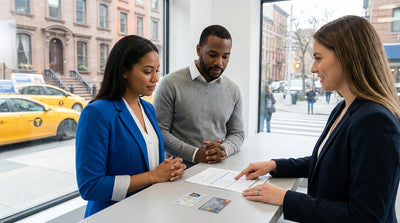 A silver car rental driving across the Brooklyn Bridge with the sunny New York City skyline in the background