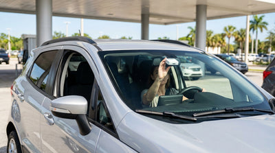 A silver car rental driving under a green SunPass toll gantry on a sunny highway in Florida