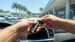 Hand holding a car rental key fob next to a parked vehicle on a sunny street in Miami