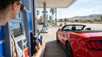 A person refueling their white car rental at a gas station pump on a sunny day in California