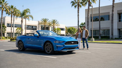 A convertible car hire driving on a sunny, winding coastal road along the Big Sur coastline in California
