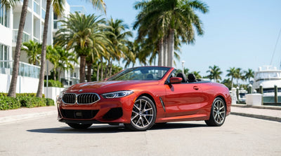 A white sports car rental driving past colorful art deco buildings on Miami's famous Ocean Drive